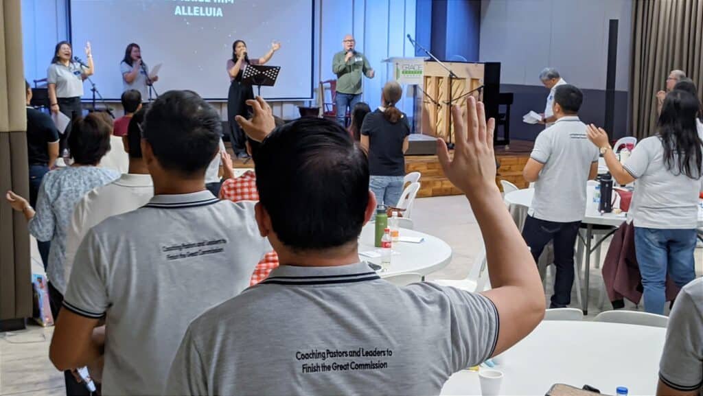 A T-Net Philippines National Gathering with a group of people in a room, featuring a woman with a microphone on stage.