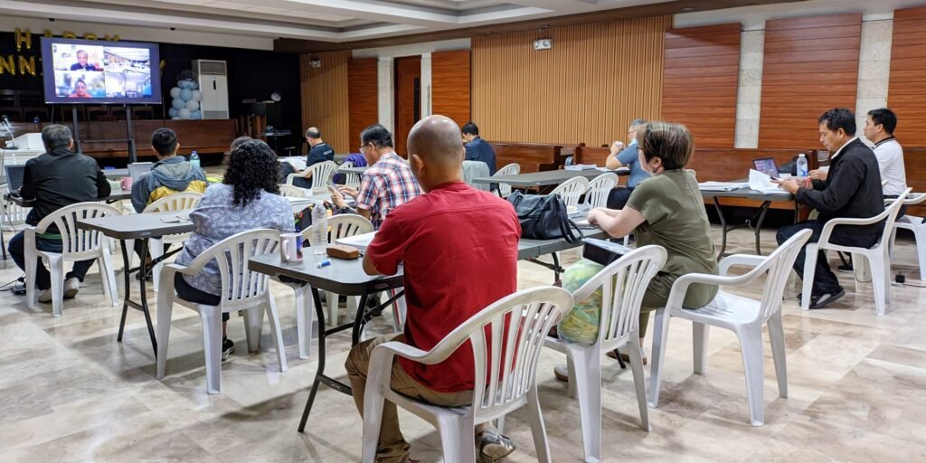 People sitting at tables in a conference hall watching a presentation on a screen.